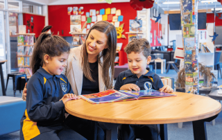 A photo of two St Paul of the Cross Catholic Primary School Dulwich Hill students and Principal Watson reading in the library and on their journey to 2025 NAPLAN results success